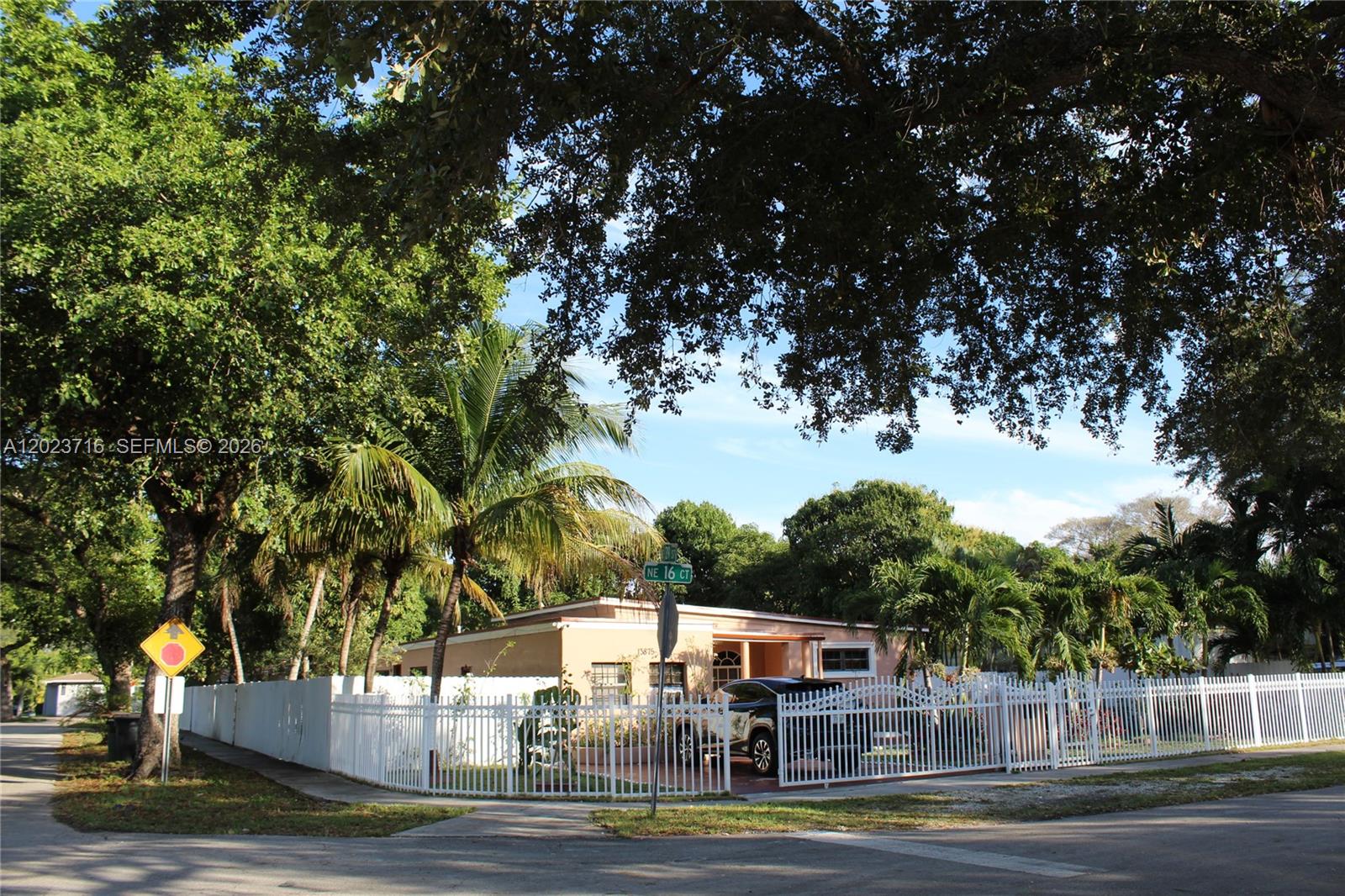 A single-story house with a white fence and palm trees stands on a corner lot — 13875 NE 16th Ct, North Miami FL 33181, NORTH MIAMI, FL