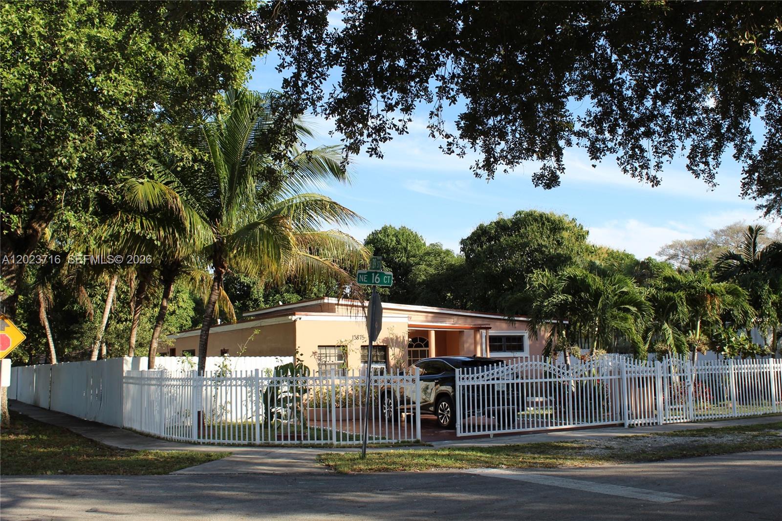 A single-story tan house with a white fence and a car parked in the driveway — 13875 NE 16th Ct, North Miami FL 33181, NORTH MIAMI, FL