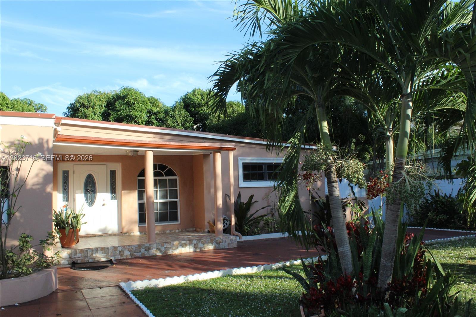 A peach-colored single-story house features a covered front porch with columns and palm trees — 13875 NE 16th Ct, North Miami FL 33181, NORTH MIAMI, FL