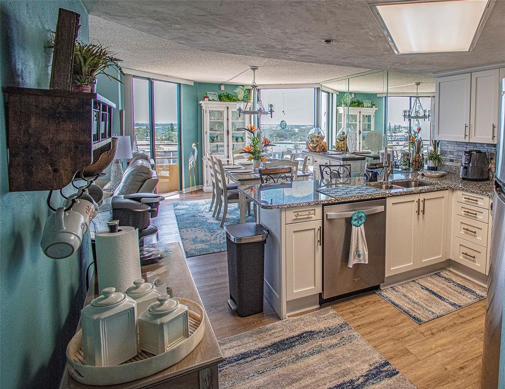 An open-concept kitchen and dining area features white cabinets, granite countertops, and teal walls — 3023 S ATLANTIC AVENUE UNIT 507, DAYTONA BEACH SHORES, FL