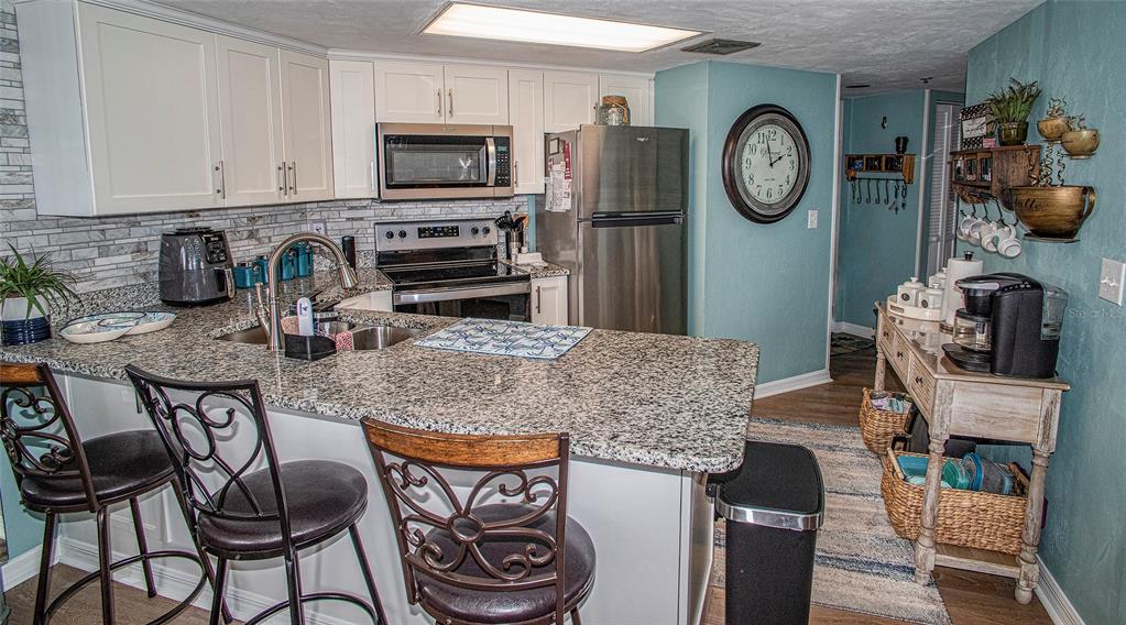 A kitchen features granite countertops, stainless steel appliances, white cabinetry, and a breakfast bar — 3023 S ATLANTIC AVENUE UNIT 507, DAYTONA BEACH SHORES, FL