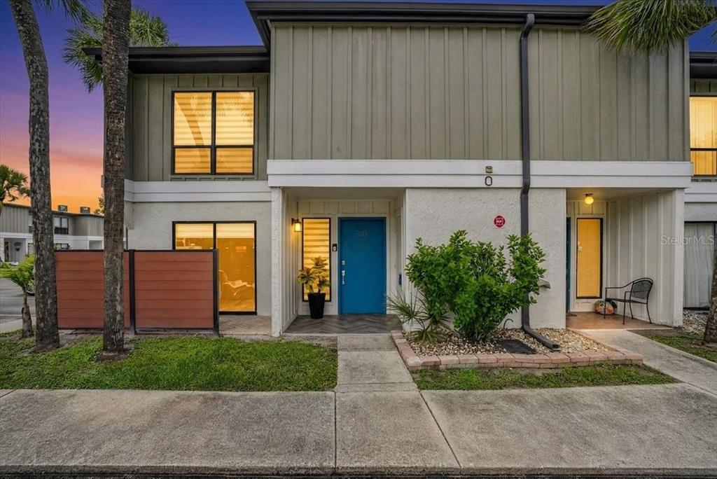A two-story townhouse exterior with a blue front door, vertical siding, and a small garden — 4001 BENEVA ROAD UNIT 310, SARASOTA, FL