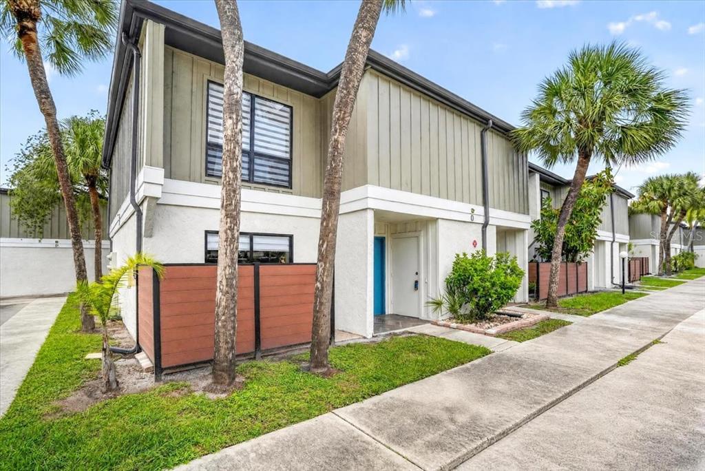 A two-story townhouse exterior features light-colored stucco, vertical siding, a small patio, and palm trees — 4001 BENEVA ROAD UNIT 310, SARASOTA, FL