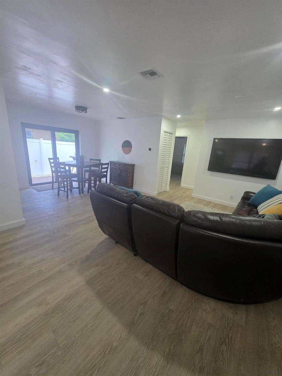 A living room with light wood-look flooring, a dark leather sectional, and an adjacent dining area — 320 Sterling Avenue, Delray Beach FL 33444, DELRAY BEACH, FL