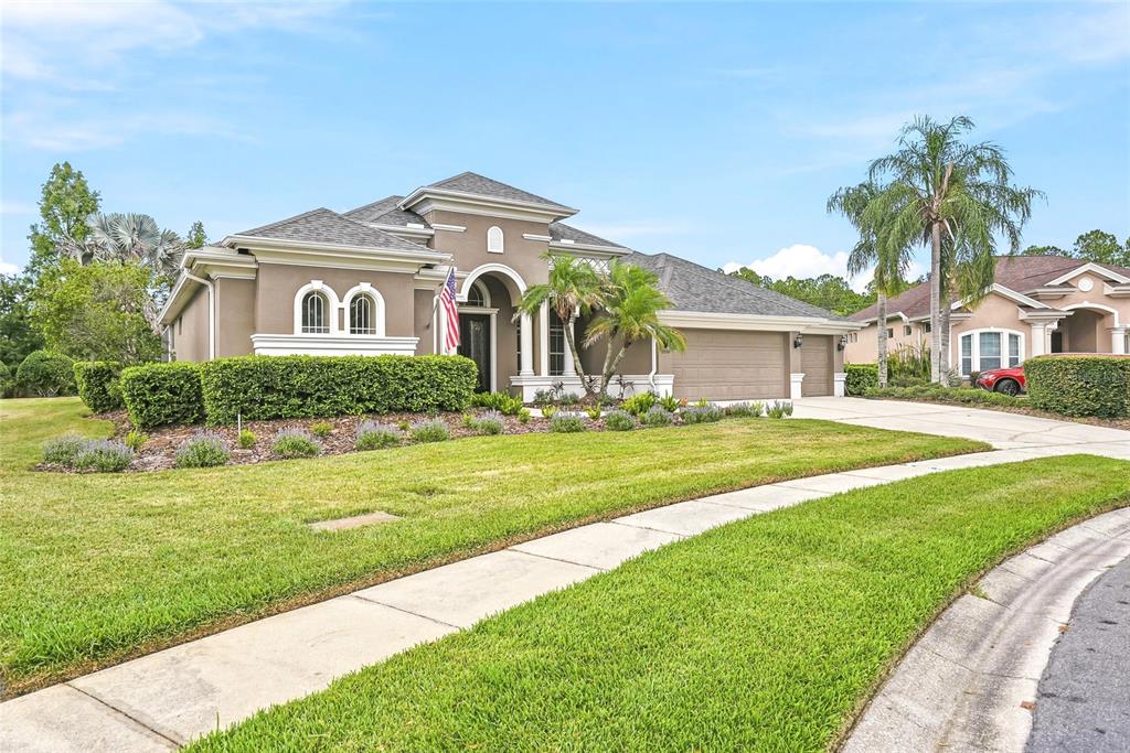 A single-story tan house with a three-car garage and a manicured lawn — 23534 GRACEWOOD CIRCLE, LAND O LAKES, FL