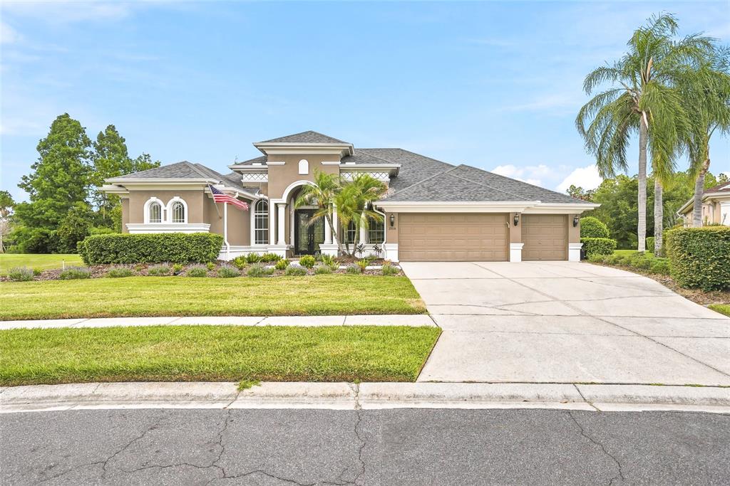 A single-story house with a tan stucco exterior, a three-car garage, and a palm tree — 23534 GRACEWOOD CIRCLE, LAND O LAKES, FL