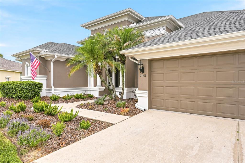 A tan house exterior features a two-car garage, a palm tree, and a front walkway — 23534 GRACEWOOD CIRCLE, LAND O LAKES, FL