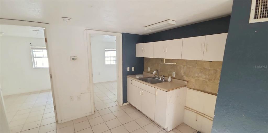 A kitchen with white cabinets, a stainless steel sink, and tiled walls and floors — 1672 10TH STREET, SARASOTA, FL