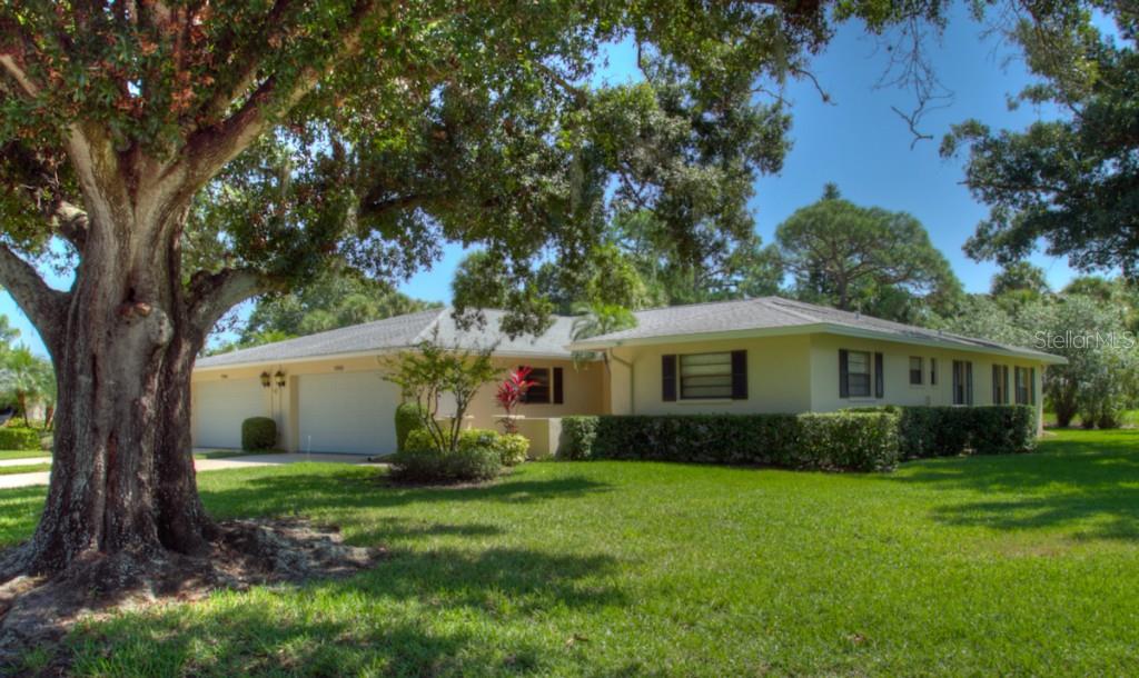 A single-story house with a light-colored exterior, a two-car garage, and a large front tree — 7093 FAIRWAY BEND LANE, SARASOTA, FL