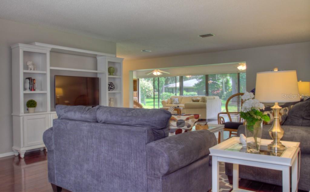A living room features a white entertainment center, dark sofa, and a view of a sunroom — 7093 FAIRWAY BEND LANE, SARASOTA, FL