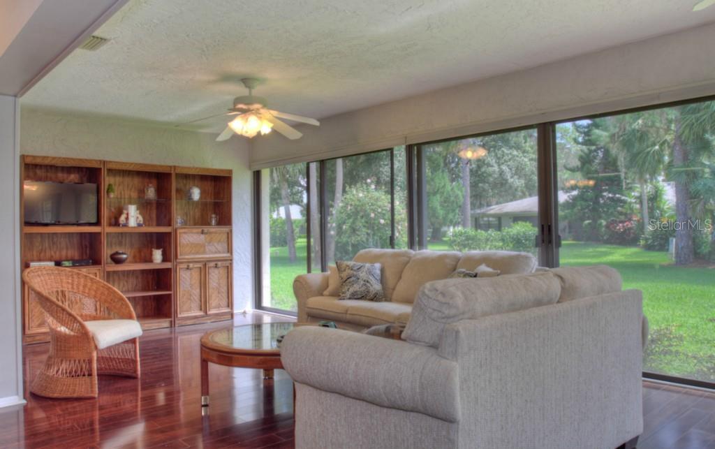 A living room with hardwood floors, a wicker chair, a beige sofa, and large windows — 7093 FAIRWAY BEND LANE, SARASOTA, FL