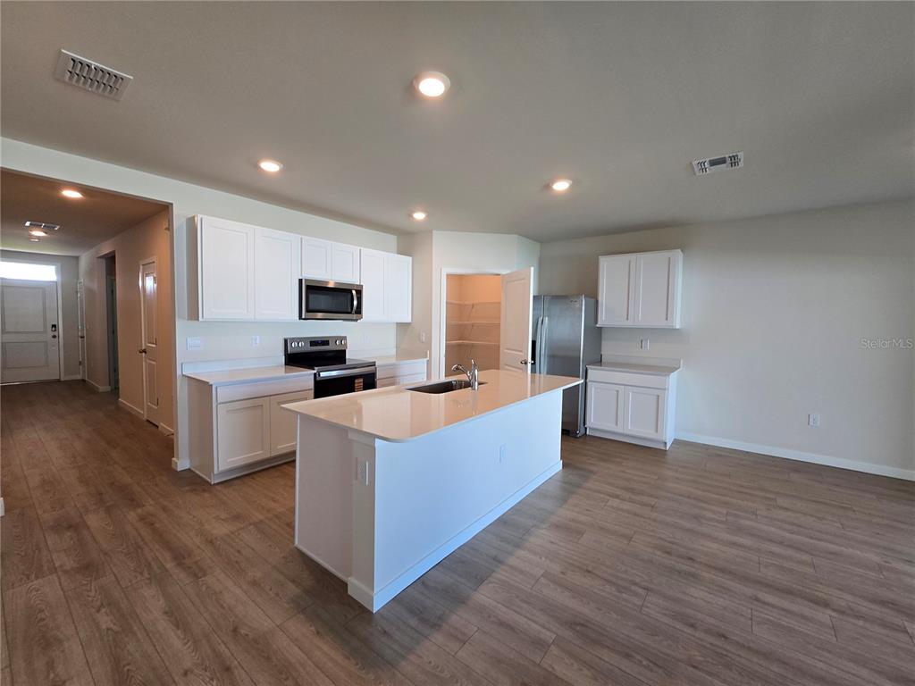 A kitchen features white cabinets, a central island with a sink, and light wood flooring — 9489 TURTLE GRASS CIRCLE, PUNTA GORDA, FL