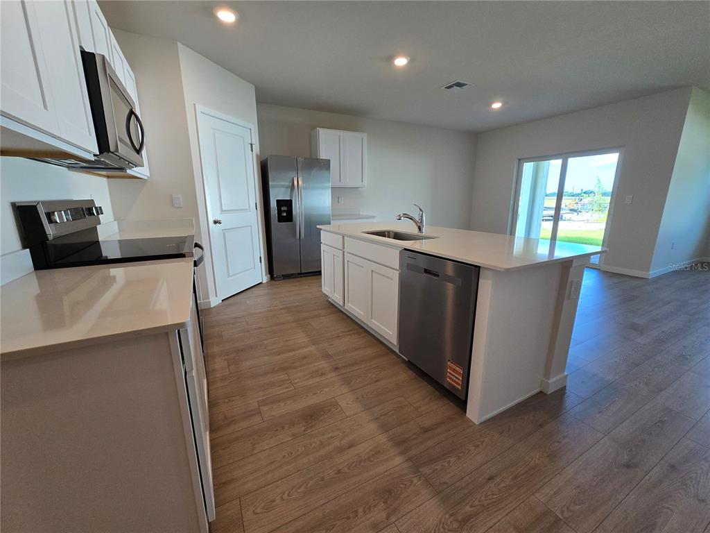 A modern kitchen features white cabinetry, stainless steel appliances, a center island, and wood-look flooring — 9489 TURTLE GRASS CIRCLE, PUNTA GORDA, FL