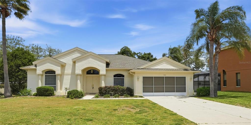 A single-story house with a beige stucco exterior, a screened garage, and two palm trees — 7221 ALOE DRIVE, SPRING HILL, FL
