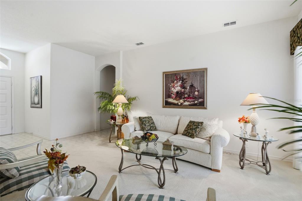 A living room features a white sofa, glass-topped tables, and a large floral wall painting — 7221 ALOE DRIVE, SPRING HILL, FL