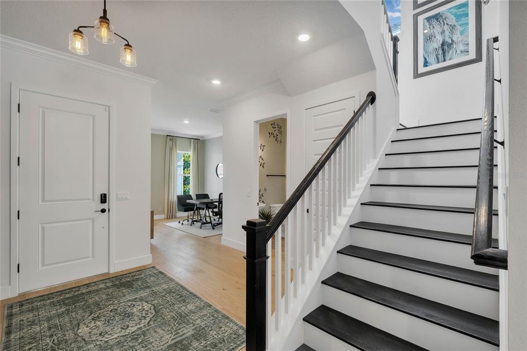 An entryway features a staircase with black treads, white walls, and a light wood floor — 17434 HONEYBELL TANGELO COURT, WINTER GARDEN, FL