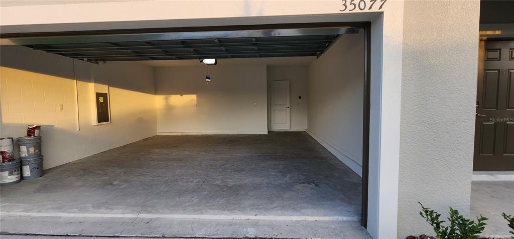 An open, empty two-car garage with white walls, a concrete floor, and a side door — 35077 ACKLEY TRACE, ZEPHYRHILLS, FL