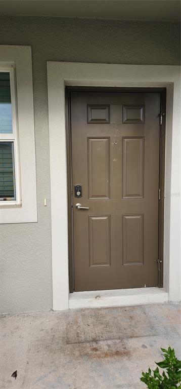 A brown six-panel front door with a digital keypad lock is set in a white frame — 35077 ACKLEY TRACE, ZEPHYRHILLS, FL