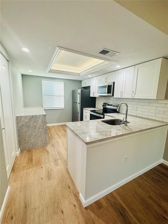 A kitchen features white cabinets, granite countertops, stainless steel appliances, and light wood-look flooring — 203 MEADOW LANE, OLDSMAR, FL