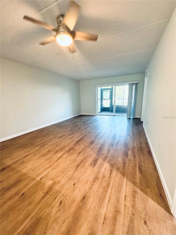 An empty living room features wood-look flooring, a ceiling fan, and a sliding glass door — 203 MEADOW LANE, OLDSMAR, FL