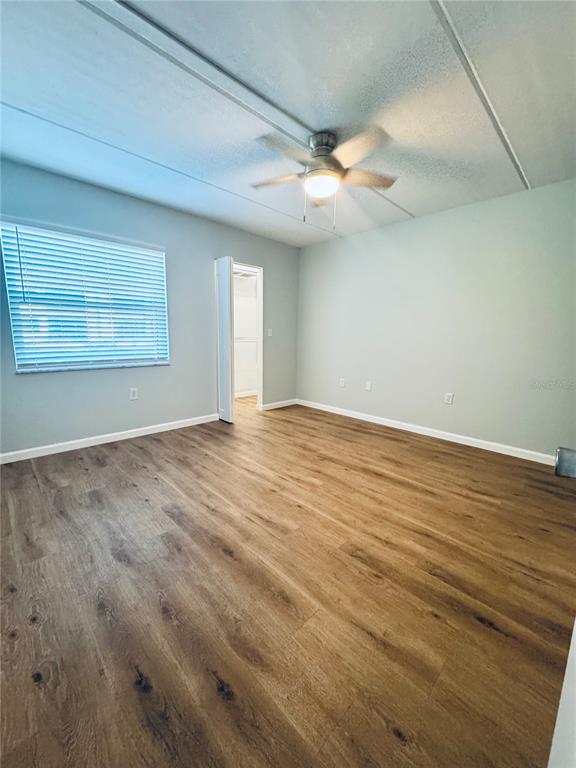 An empty room features light-colored walls, wood-look flooring, a ceiling fan, and a window — 203 MEADOW LANE, OLDSMAR, FL