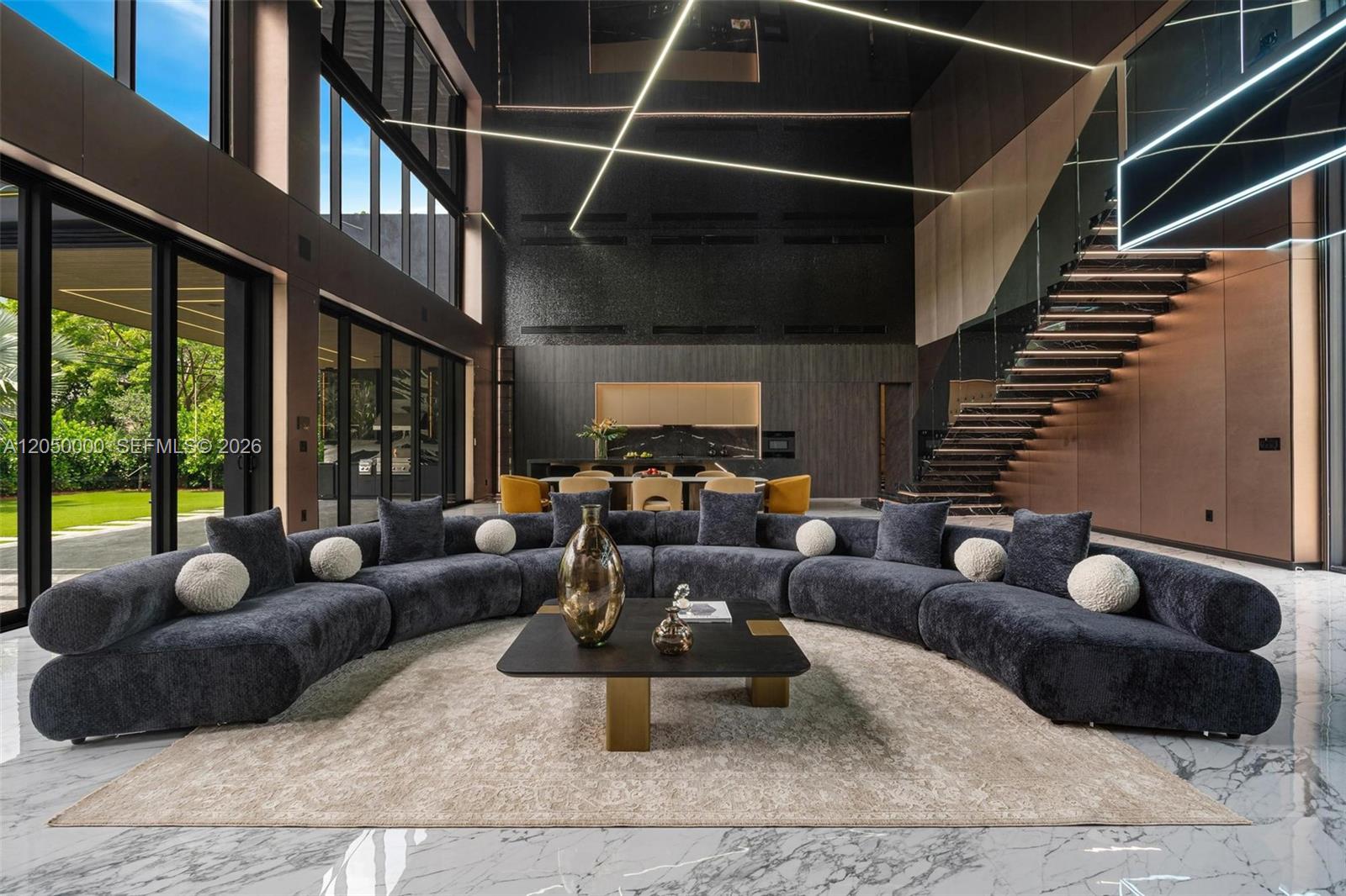 A modern living room features a large curved sofa, marble floors, and a floating staircase — 13500 SW 69th Ave, Pinecrest FL 33156, PINECREST, FL