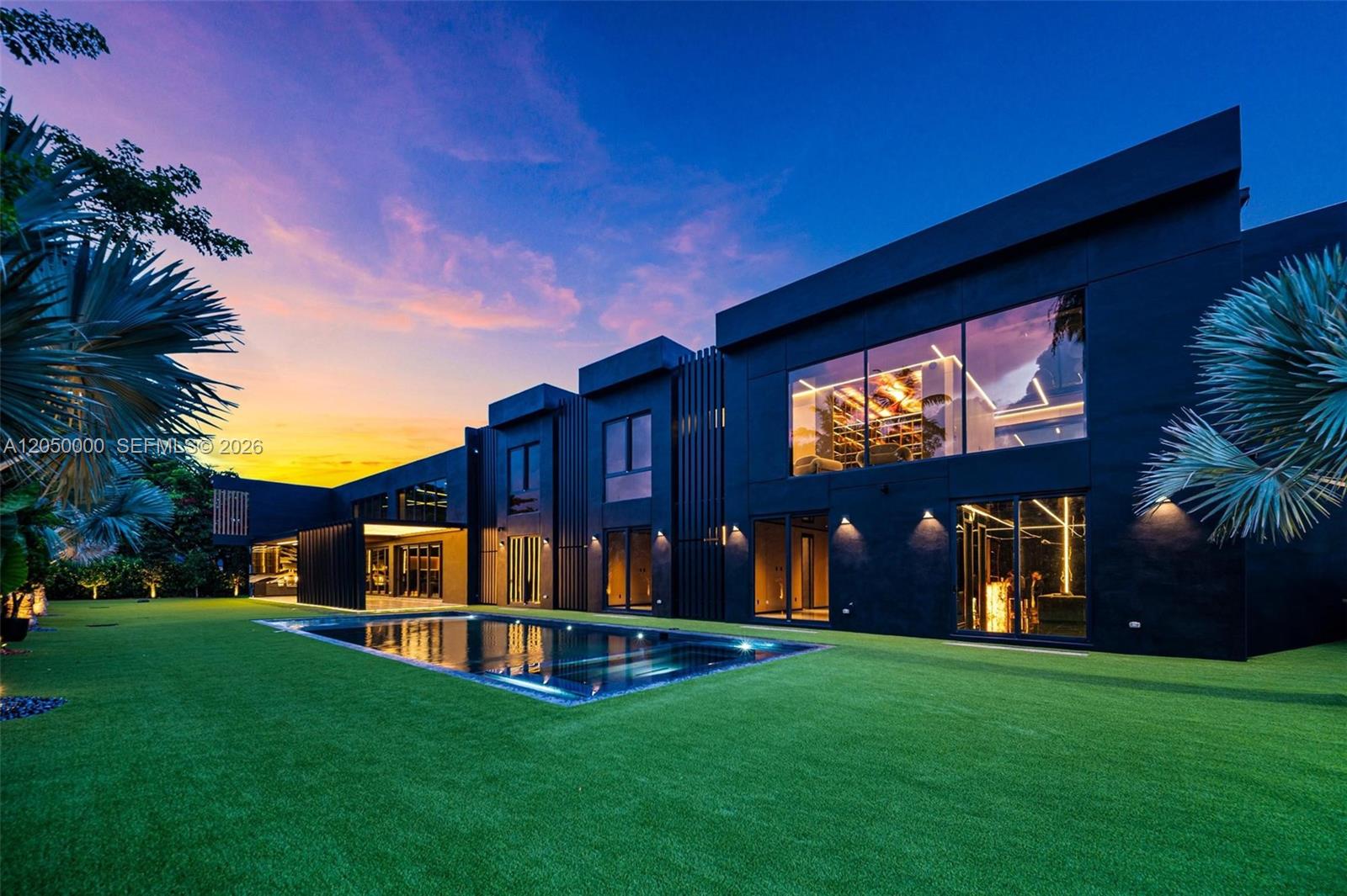 A modern black two-story house features a rectangular swimming pool set in a grassy yard — 13500 SW 69th Ave, Pinecrest FL 33156, PINECREST, FL