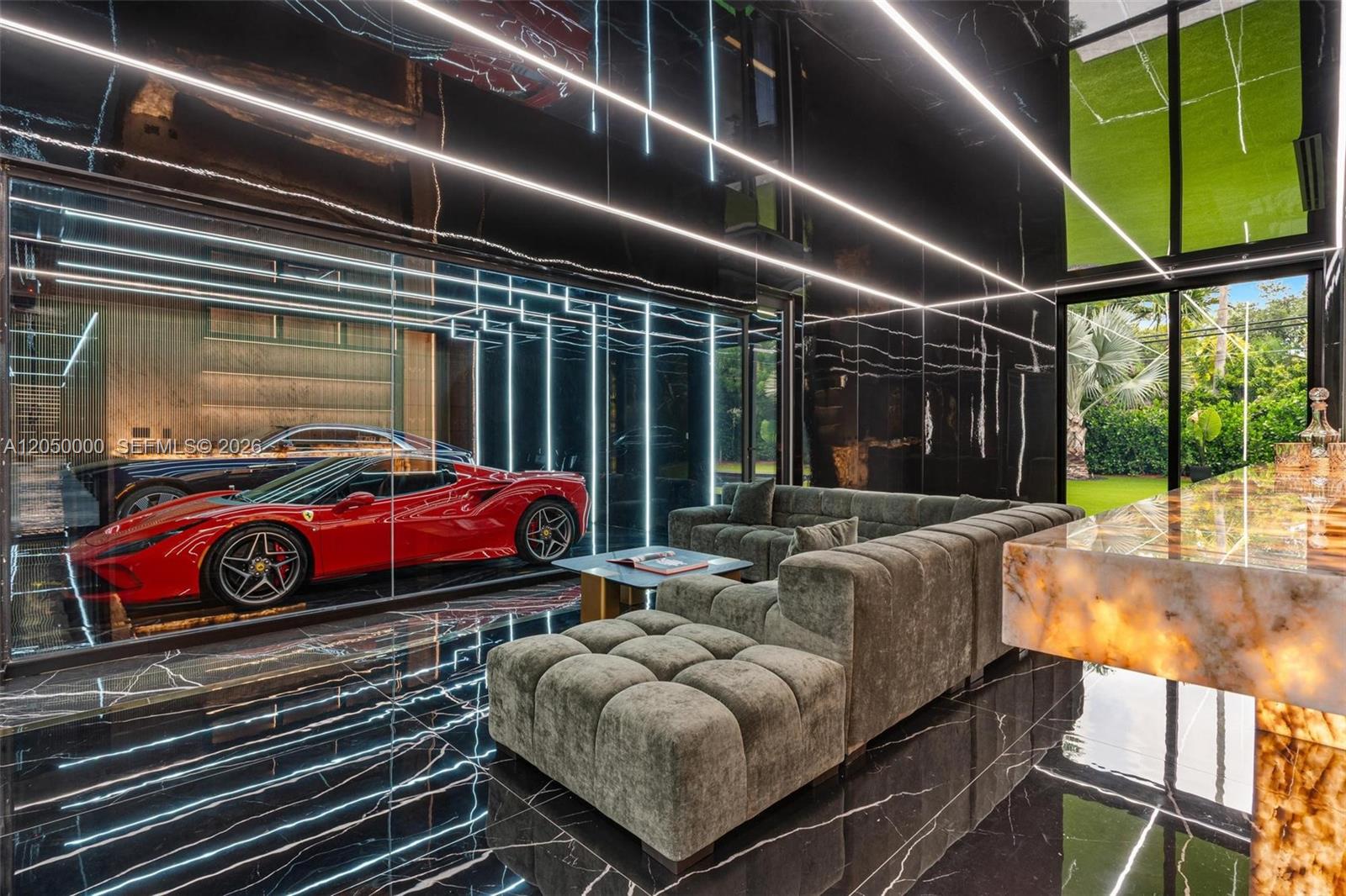 A modern lounge features a glass-walled garage displaying a red Ferrari, black marble floors, and lighting — 13500 SW 69th Ave, Pinecrest FL 33156, PINECREST, FL