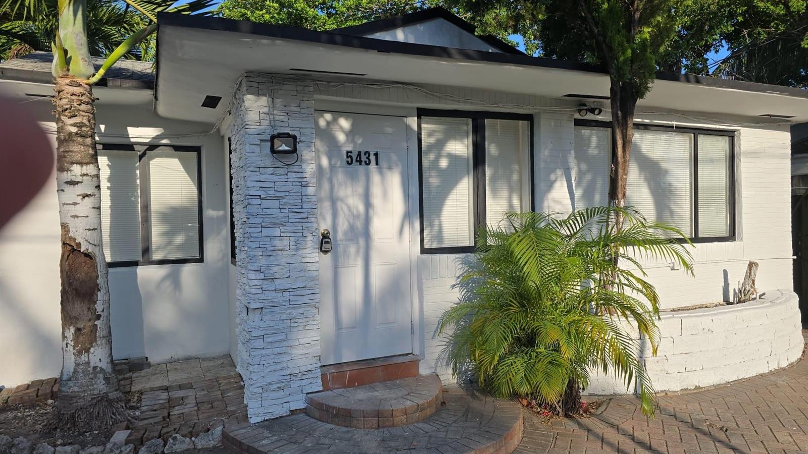 A white house exterior features a stone-accented entryway, a front door, and a palm tree — 5431 NW 30th Avenue, Miami FL 33142, MIAMI, FL