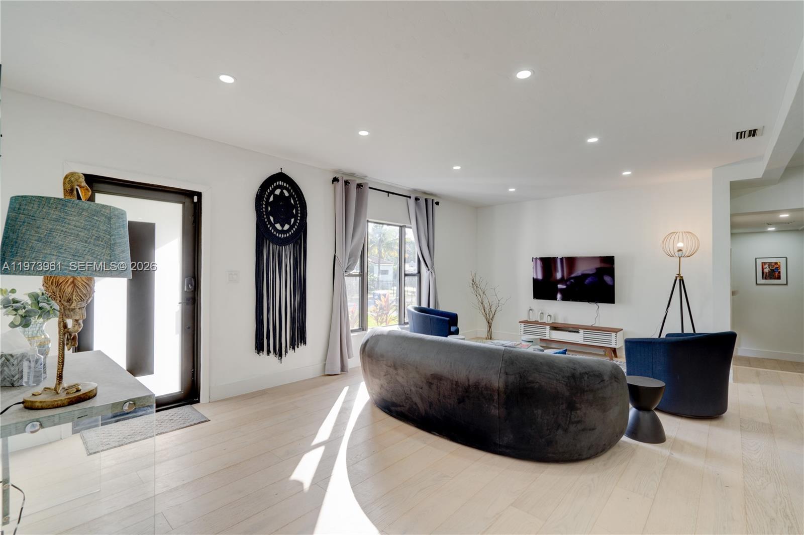A modern living room features a curved sofa, two blue armchairs, and light wood flooring — 347 NE 110th St, Miami FL 33161, MIAMI, FL