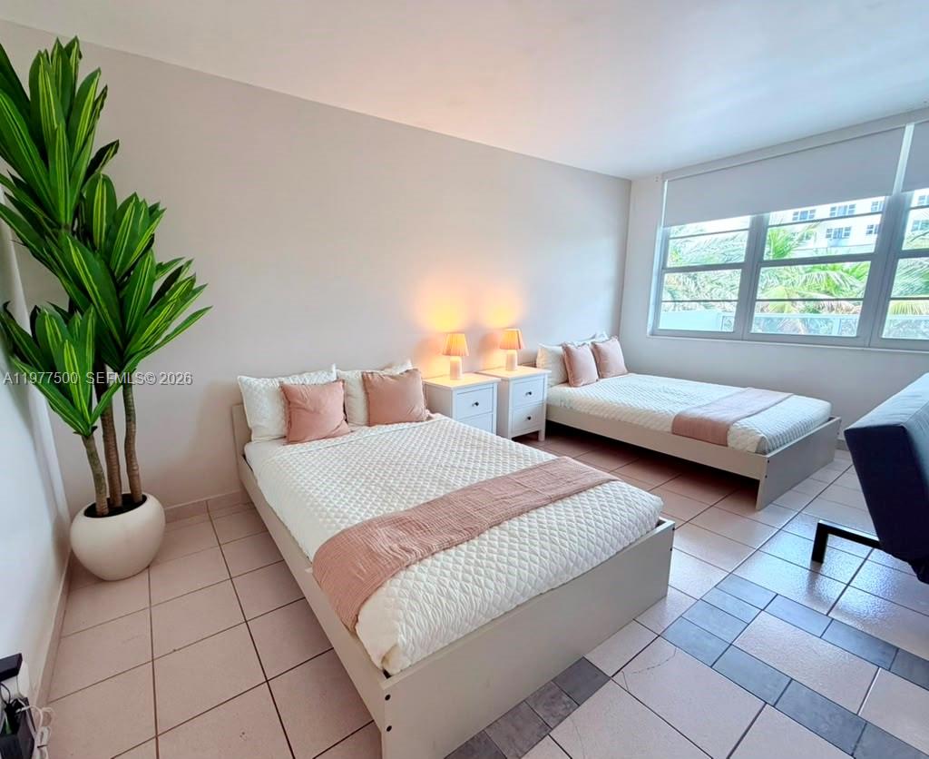 A bedroom features two beds, two nightstands with lamps, a large plant, and tiled floors — 100 Lincoln Rd # 304, Miami Beach FL 33139, MIAMI BEACH, FL