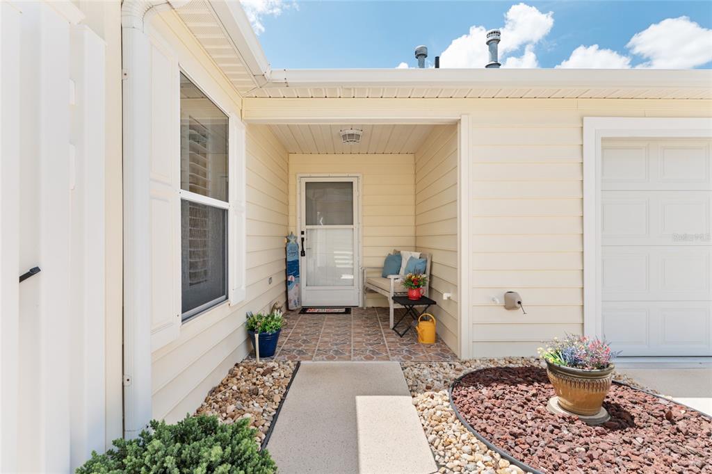 The exterior view shows a covered entryway with a tiled porch, bench, and garage door — 1492 AZTECA LOOP, THE VILLAGES, FL