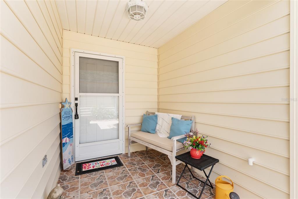 A covered porch features light yellow siding, a tiled floor, a bench, and a screen door — 1492 AZTECA LOOP, THE VILLAGES, FL