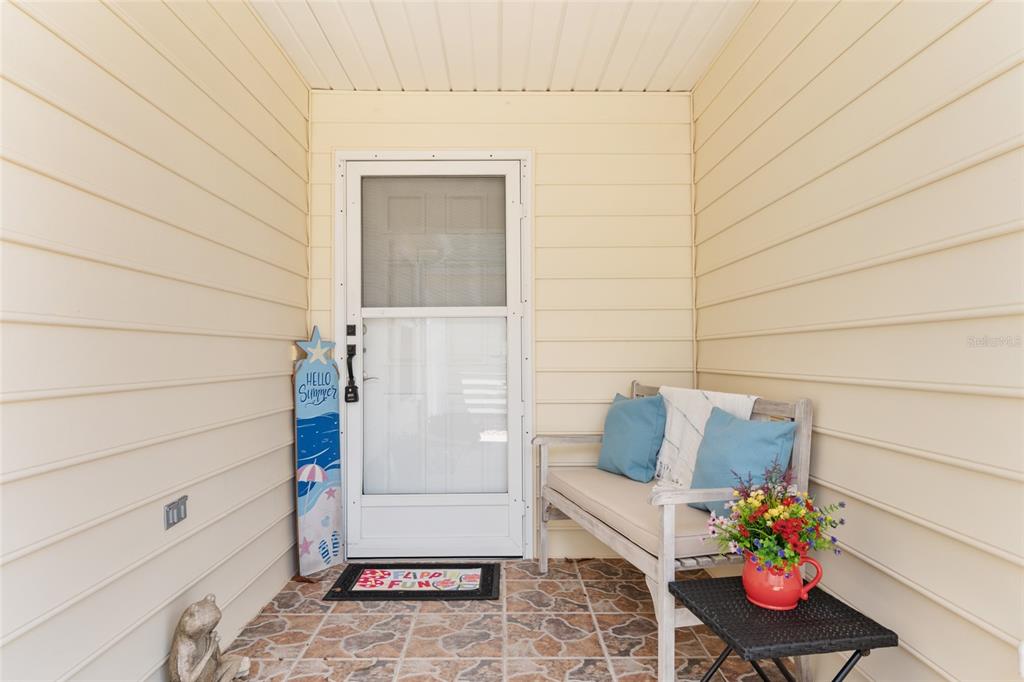 A covered front porch features a white storm door, a wooden bench, and tiled flooring — 1492 AZTECA LOOP, THE VILLAGES, FL