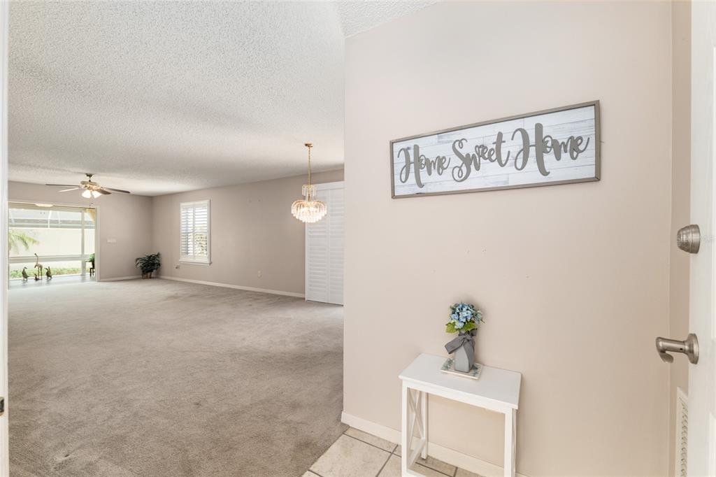 An entryway with a small table leads into a carpeted living area with a chandelier — 1492 AZTECA LOOP, THE VILLAGES, FL