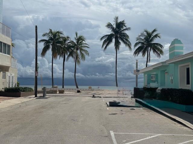 A paved parking area leads toward a beach entrance framed by palm trees and buildings — 308 Monroe Street, Hollywood FL 33019, HOLLYWOOD, FL