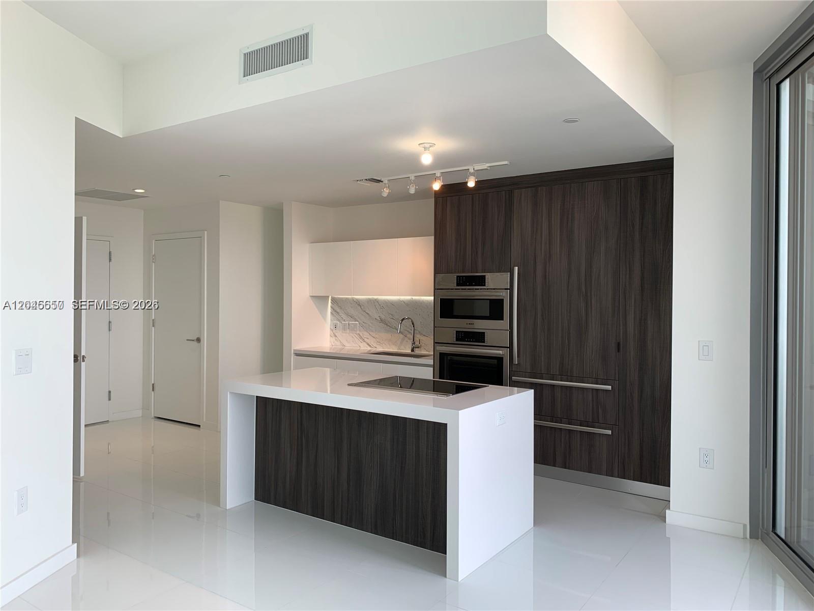 A modern kitchen features a white island, dark wood cabinetry, and stainless steel appliances — 851 NE 1st Ave # 2702, Miami FL 33132, MIAMI, FL