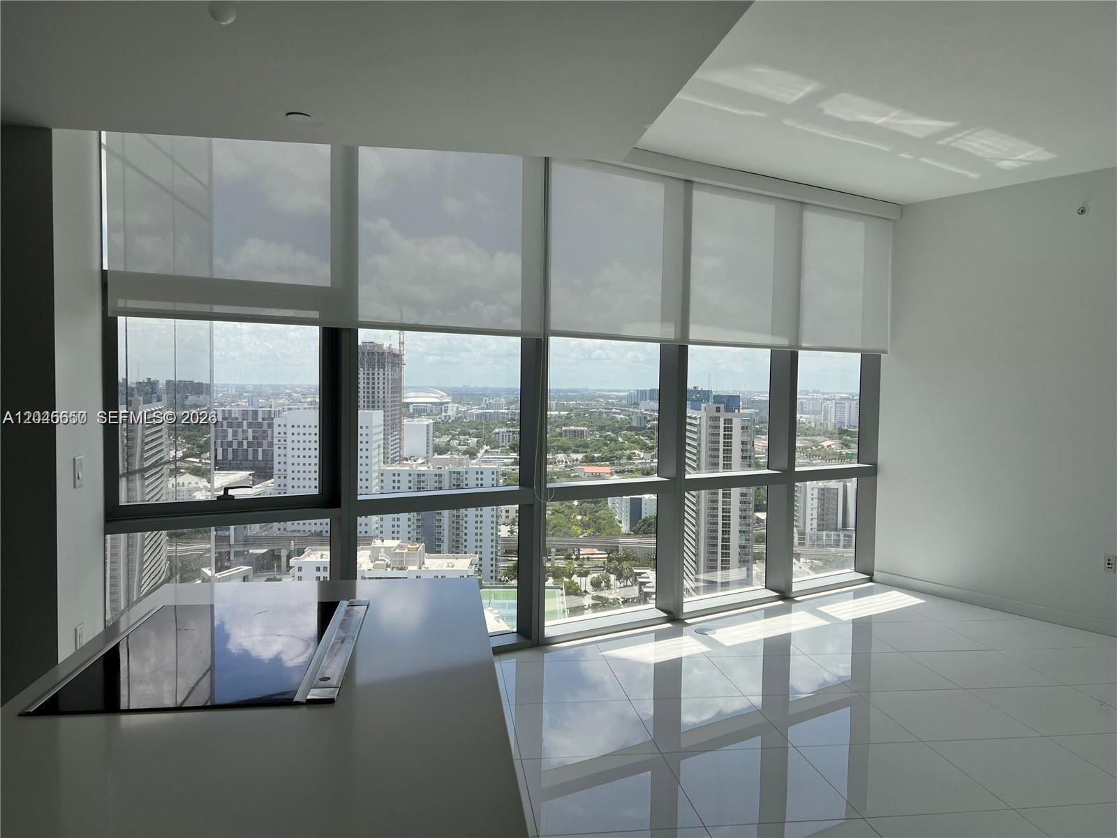 A modern kitchen area features floor-to-ceiling windows, white tile flooring, and a glass cooktop — 851 NE 1st Ave # 2702, Miami FL 33132, MIAMI, FL