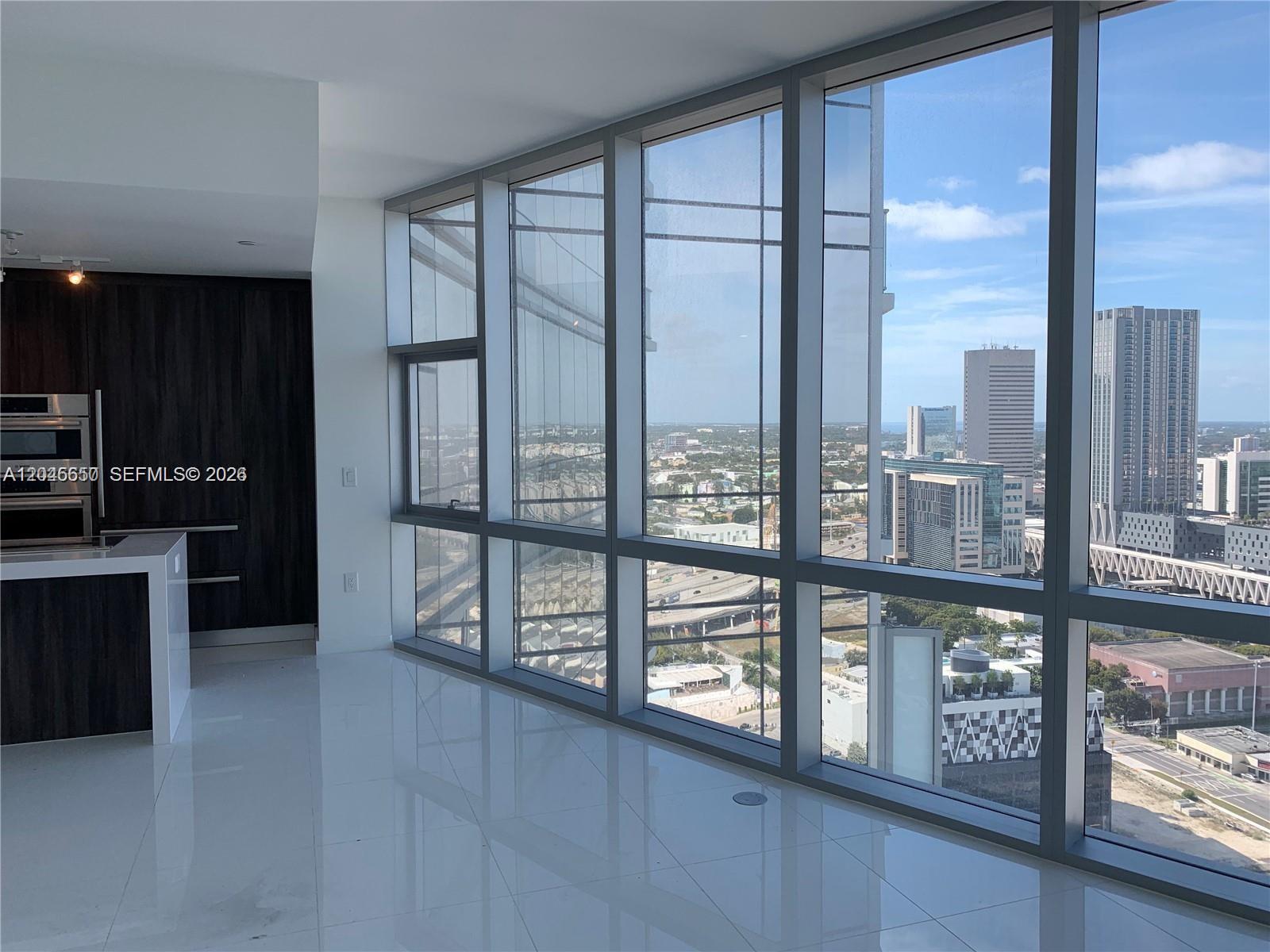 A modern kitchen with dark cabinetry and white tile floors overlooks a city skyline — 851 NE 1st Ave # 2702, Miami FL 33132, MIAMI, FL