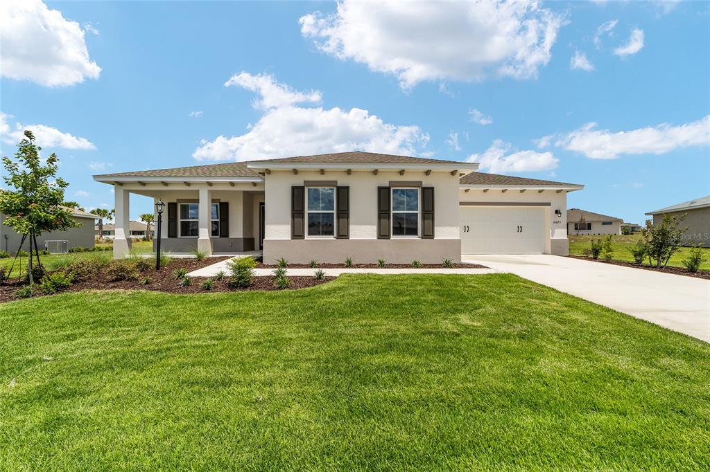 A single-story house with a beige stucco exterior, a two-car garage, and a front porch — 10673 SW 102ND LANE, OCALA, FL