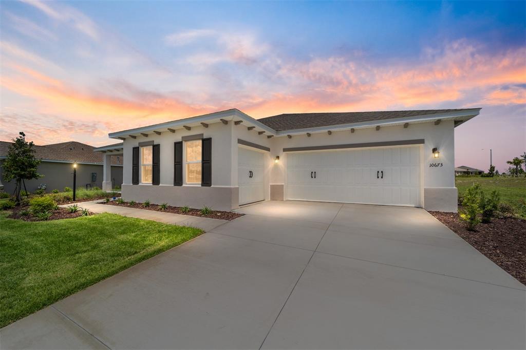 A single-story house with a white stucco exterior, dark shutters, and a three-car garage — 10673 SW 102ND LANE, OCALA, FL