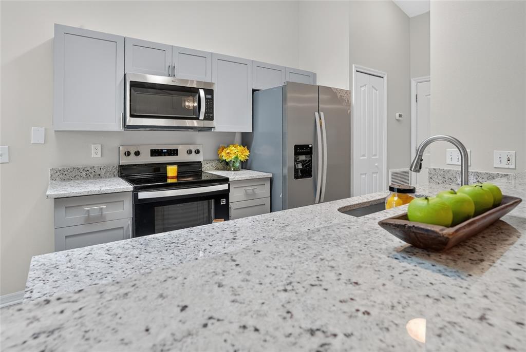 A kitchen features grey cabinets, stainless steel appliances, and speckled granite countertops — 1317 HOMEWAY LANE, DELTONA, FL
