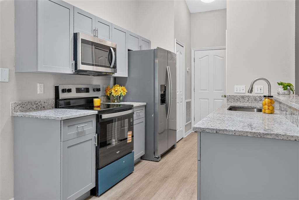 A kitchen features gray cabinets, granite countertops, stainless steel appliances, and light wood-look flooring — 1317 HOMEWAY LANE, DELTONA, FL