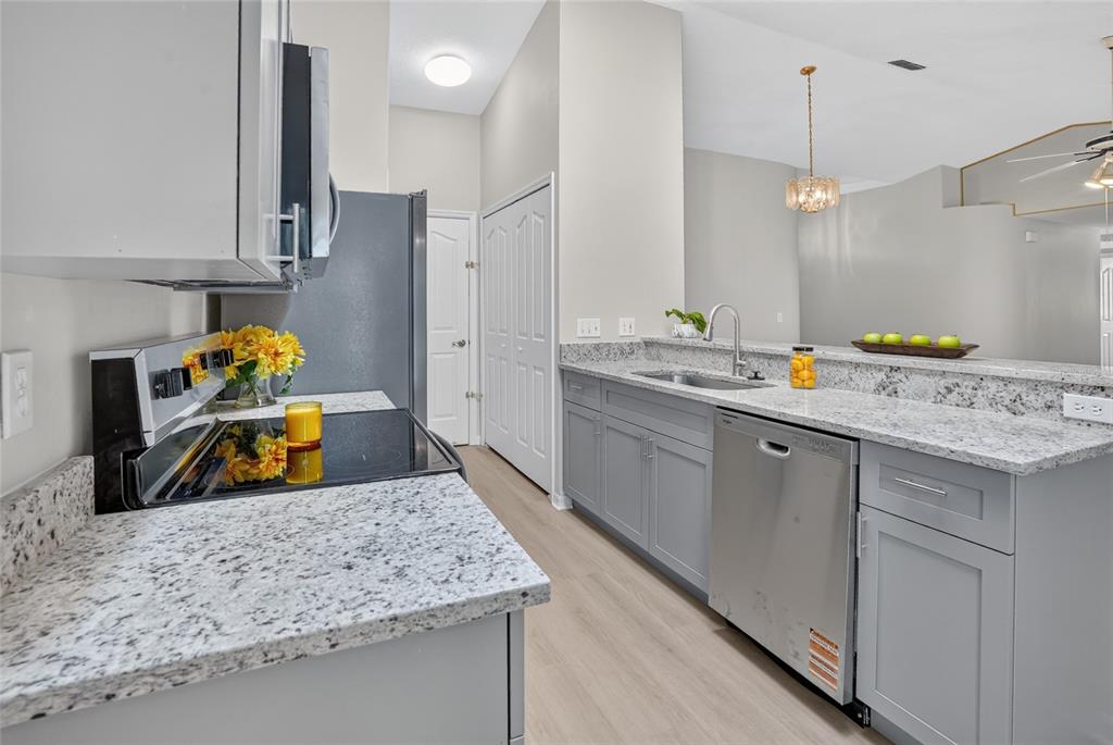 A kitchen features gray cabinets, granite countertops, stainless steel appliances, and light wood-look flooring — 1317 HOMEWAY LANE, DELTONA, FL