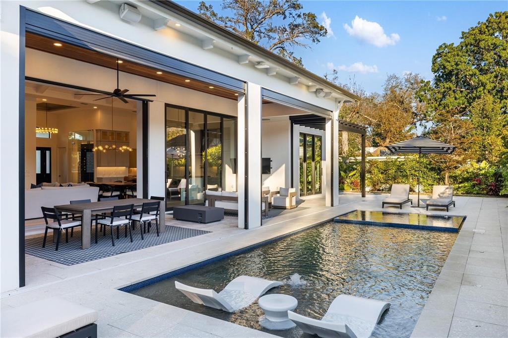 A covered patio with a dining area overlooks a swimming pool with in-water lounge chairs — 1800 WEBBER STREET, SARASOTA, FL