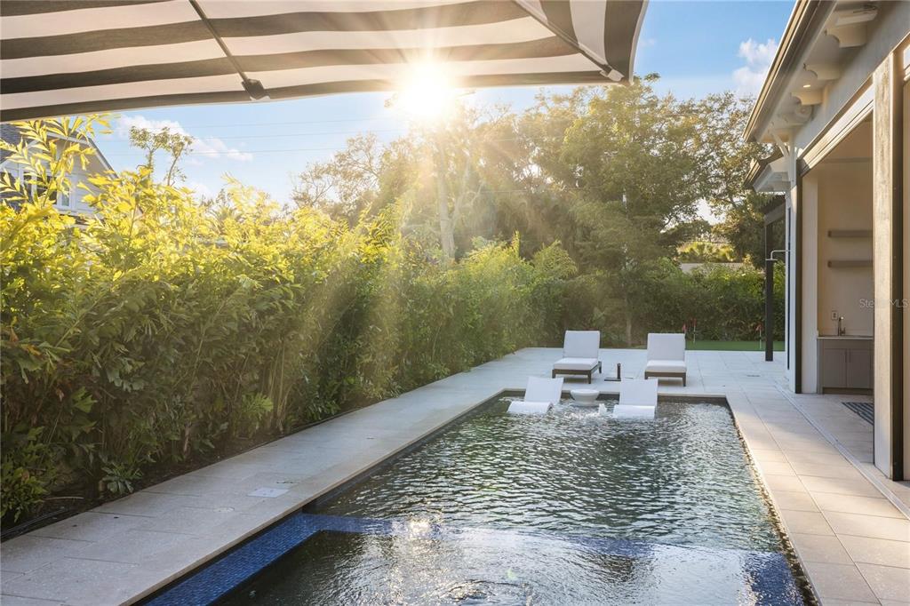A backyard swimming pool with lounge chairs sits beside a patio under a striped umbrella — 1800 WEBBER STREET, SARASOTA, FL