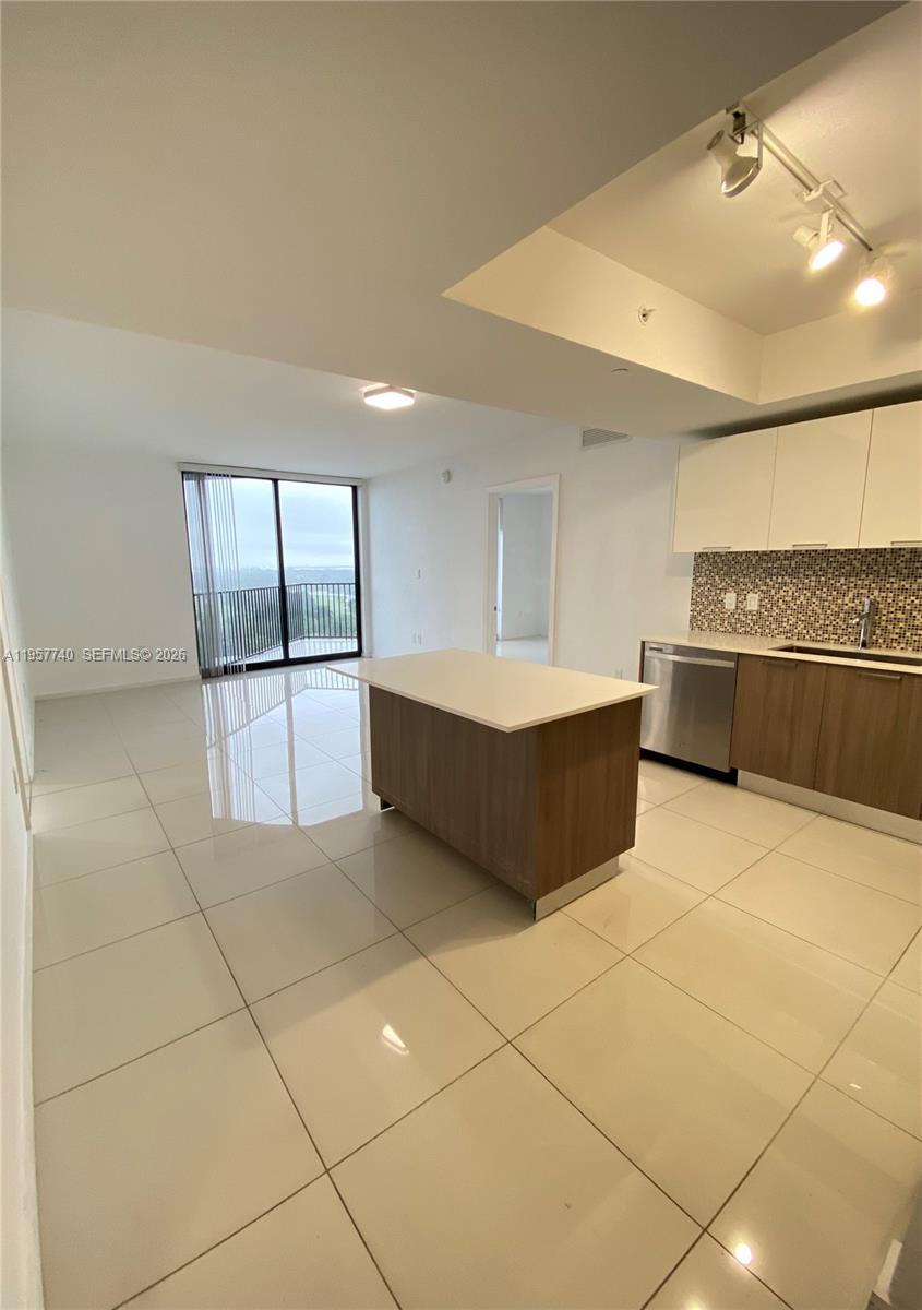 A modern kitchen with an island and white tile floors opens to a living area — 5252 NW 85th Ave # 910, Doral FL 33166, DORAL, FL