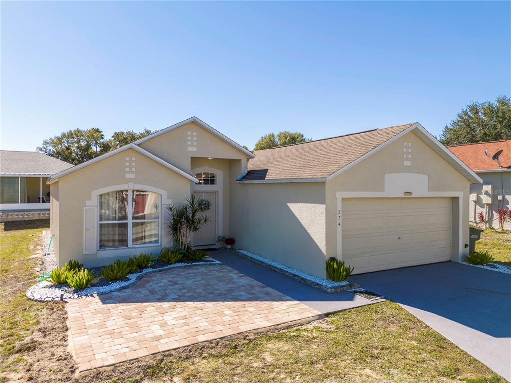 A single-story house with a beige stucco exterior, a two-car garage, and a paver walkway — 50989 HIGHWAY 27 UNIT 274, DAVENPORT, FL