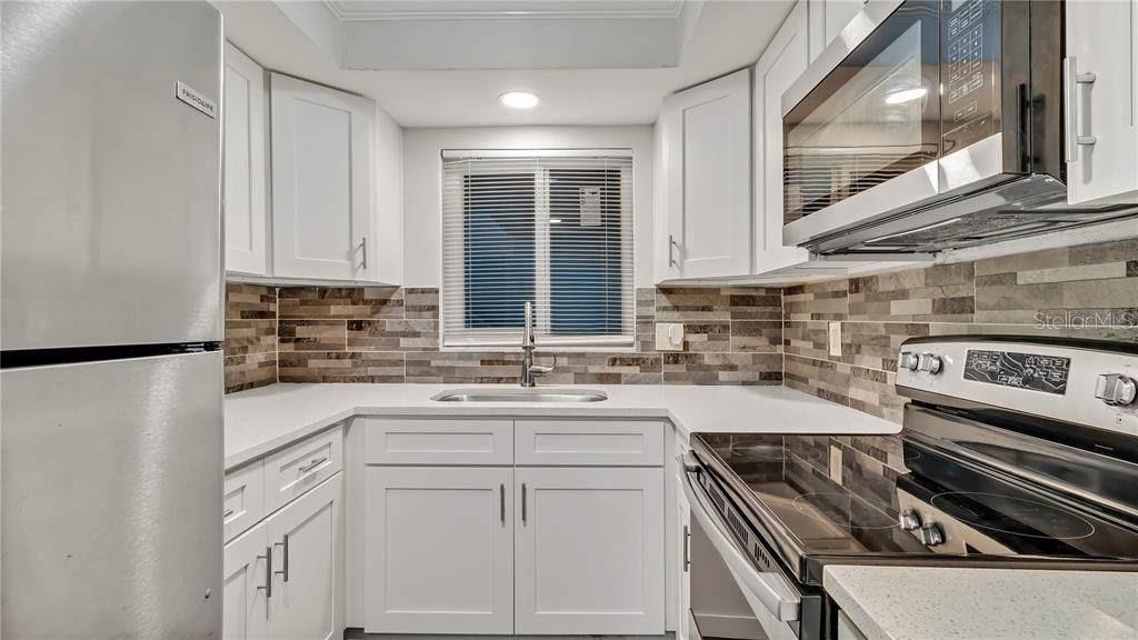 A kitchen features white cabinets, stainless steel appliances, and a stone tile backsplash — 5900 22ND AVENUE N UNIT 8, ST PETERSBURG, FL