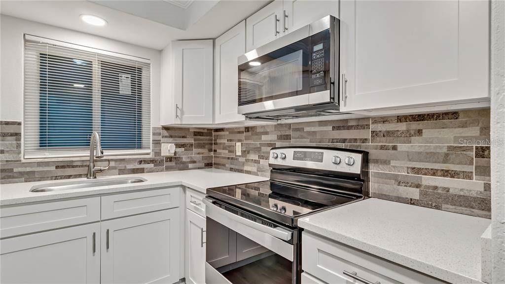 A kitchen features white cabinets, a stainless steel microwave, a glass-top stove, and tiled backsplash — 5900 22ND AVENUE N UNIT 8, ST PETERSBURG, FL
